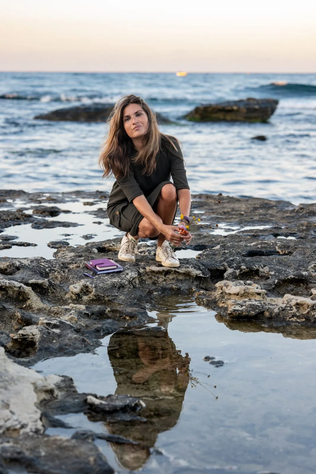 Marta holding flowers beside coastal rock pools.